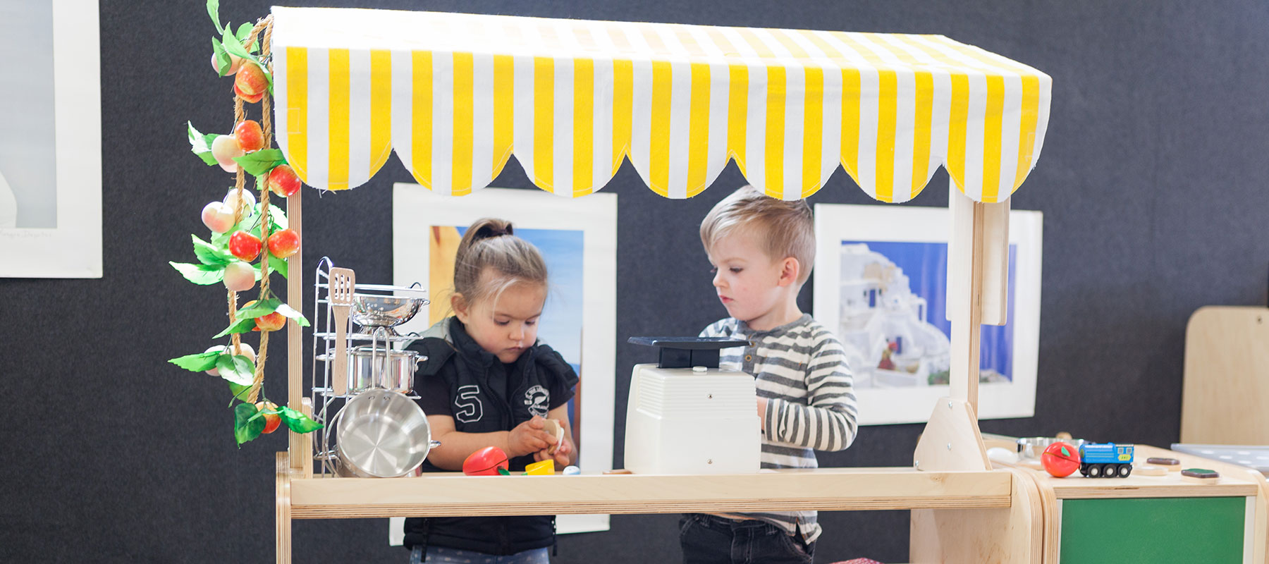 Two kids playing in a play kitchen at A pot full of colourful felt tip pens at Tadpoles Early Childhood Centre