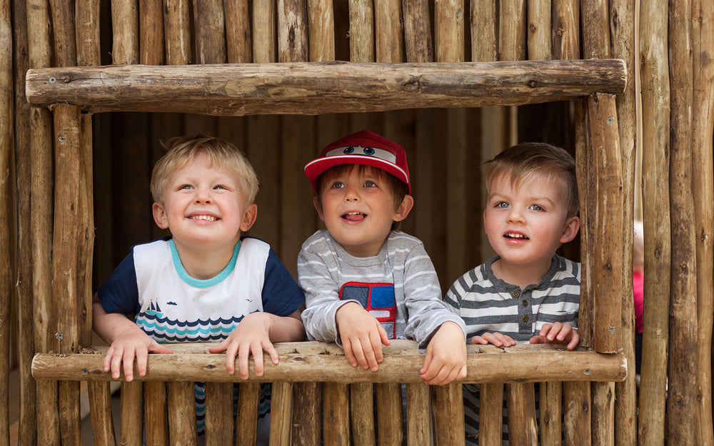 3 preschool boys smiling from a wooden playhouse at A pot full of colourful felt tip pens at Tadpoles Early Childhood Centre