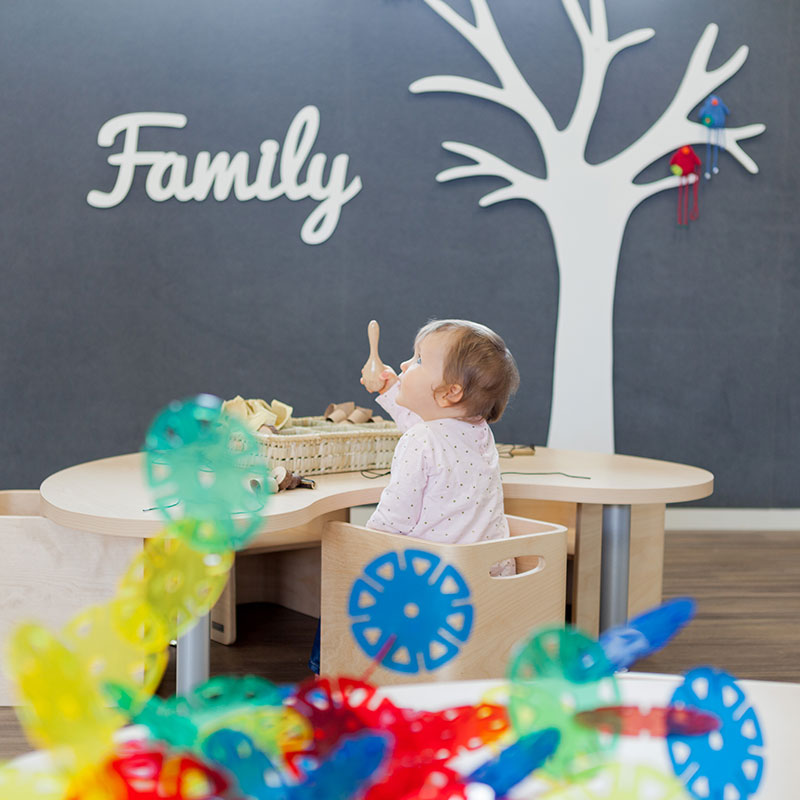 A little baby sitting at a table playing with rattle. The word Family appears on the wall at A pot full of colourful felt tip pens at Tadpoles Early Childhood Centre