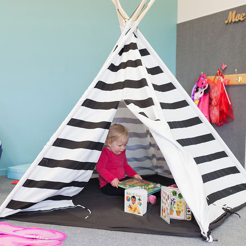A little girl playing in a black and white striped tee pee at A pot full of colourful felt tip pens at Tadpoles Early Childhood Centre