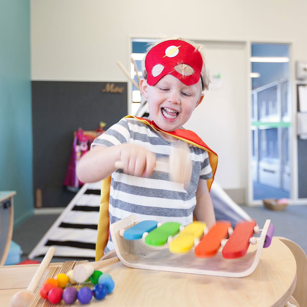 A little boy with a red mask hammering a wooden xylophone at A pot full of colourful felt tip pens at Tadpoles Early Childhood Centre