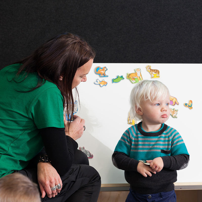 A teacher talking to a small boy at a whiteboard at A pot full of colourful felt tip pens at Tadpoles Early Childhood Centre