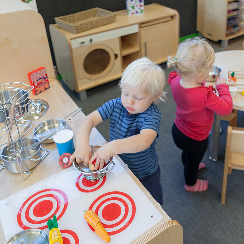 A boy and girl playing with a toy stove at A pot full of colourful felt tip pens at Tadpoles Early Childhood Centre